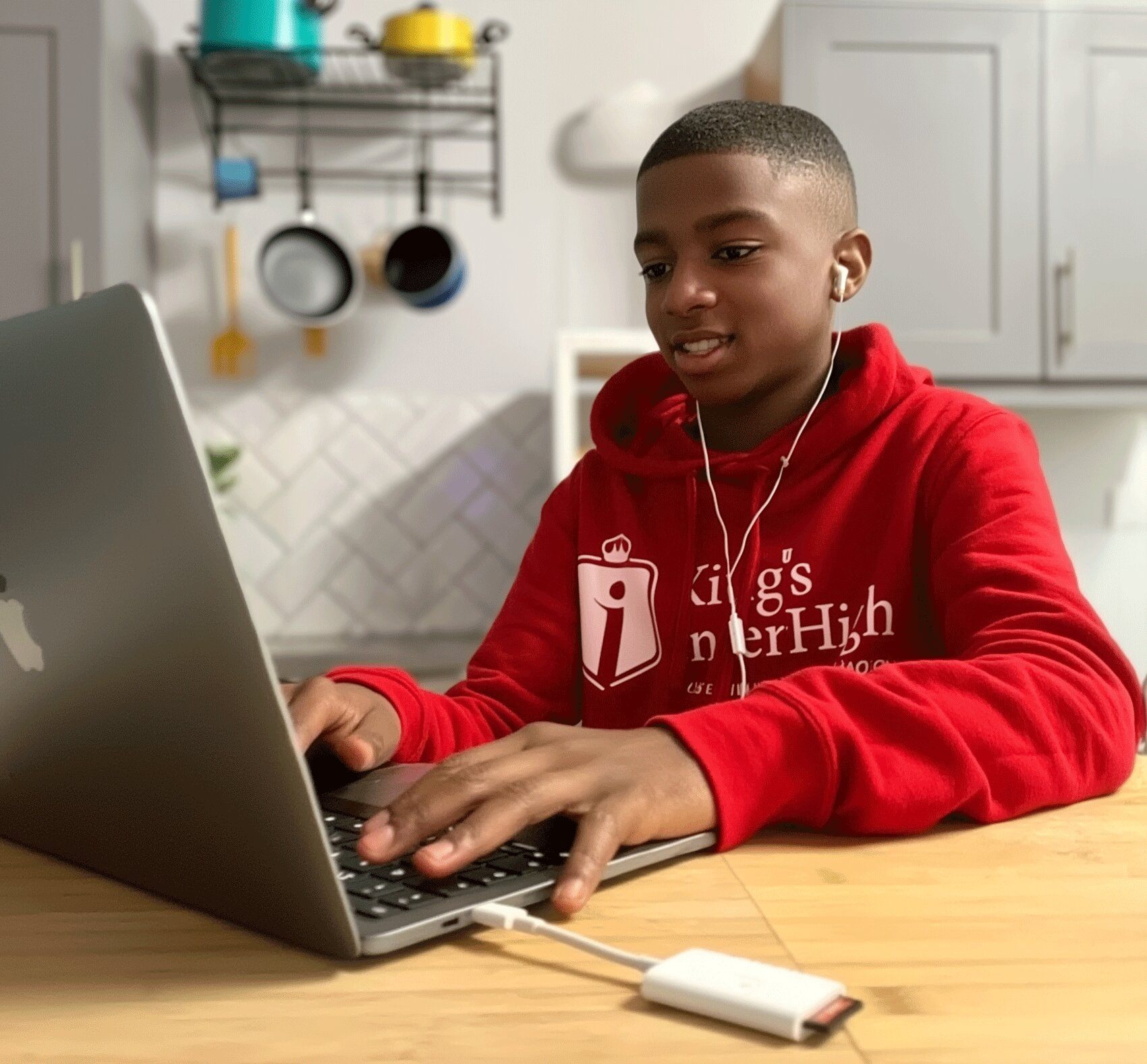 A young student wearing a red hoodie and earphones, focused on an online golf lesson at home, using a laptop.