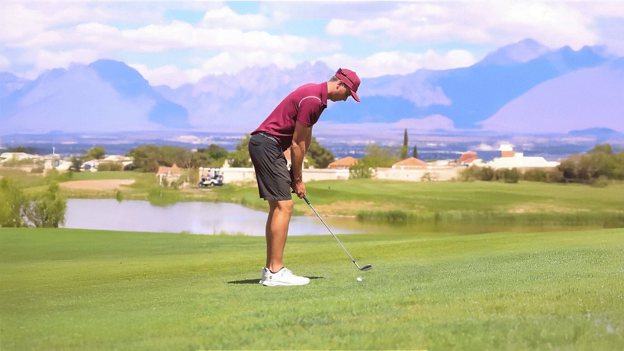 Young male golfer at the American Golf Academy’s Junior Golf Academy preparing a shot on a lush green fairway with scenic mountains and a lake in the background.